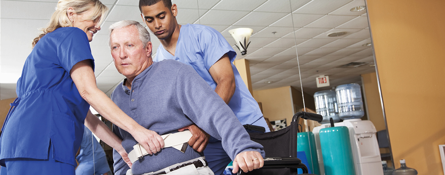 Zwei Pfleger haben Senioren mit einem Hilfsmittel aus seinem Rollstuhl